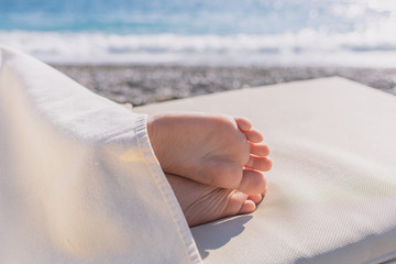 Closeup view of cute small bare feet o little caucasian child sleeping at sunny beach calmly. Legs covered with soft towel. - Powered by Adobe