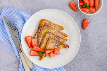 Traditional French toast sprinkled with powdered sugar with fresh strawberries on a white plate with a cup of tea. Delicious breakfast. Horizontal orientation. Top view