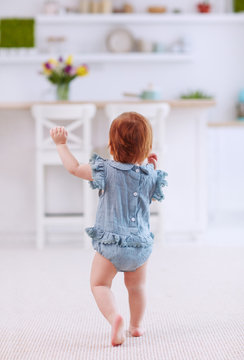 first steps of cute little baby girl in bodysuit walking away, on the carpet at home