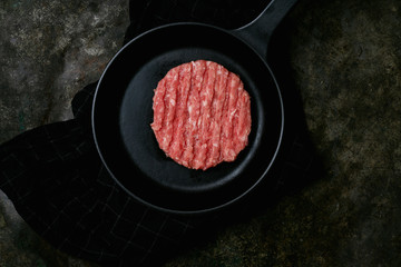 Raw Ground beef meat Burger steak cutlet served on metal frying pan over the kitchen towel. Rustic metal background. Top view