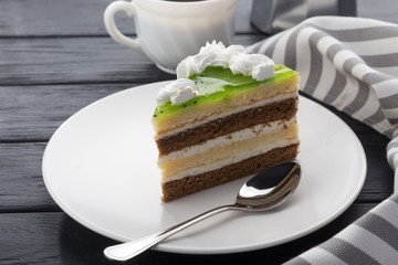 A slice of cake in a white plate on a black wooden table with a spoon, a cup of coffee, a coffee pot and a napkin. Close-up shot. Free space for text. Various slices of cakes on a plate. A piece of ch