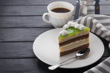 A slice of cake in a white plate on a black wooden table with a spoon, a cup of coffee, a coffee pot and a napkin. Close-up shot. Free space for text. Various slices of cakes on a plate. A piece of ch