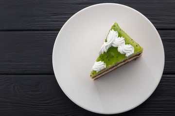 A slice of cake in a white plate on a black wooden table with a spoon, a cup of coffee, a coffee pot and a napkin. Close-up shot. Free space for text. Various slices of cakes on a plate. A piece of ch