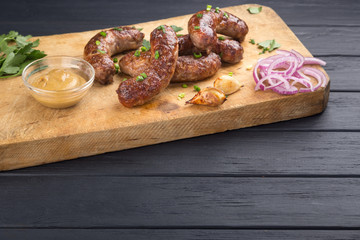 Grilled sausages from a BBQ served with a mustard, fried potatoes, garlic, herbs, beer on a wooden board all served on a black wooden table. Delicious german sausages Perfect for Octoberfest.
