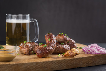 Grilled sausages from a BBQ served with a mustard, fried potatoes, garlic, herbs, beer on a wooden board all served on a black wooden table. Delicious german sausages Perfect for Octoberfest.