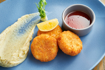 Appetizing breadcrumb shrimp croquettes with red sauce on a blue plate. Wooden background. Close up view. Tasty seafood, Film effect during post. Soft focus