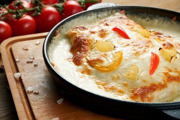 Appetizing baked pikeperch fillet in cream sauce, cheese and vegetables in a pan on a wooden background. Close up view. Tasty seafood
