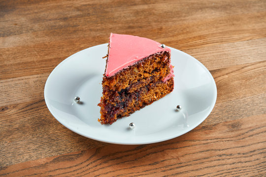 slice of biscuit cake with pink icing on a white plate on a wooden background. Bakery food photo