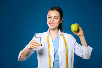 Nutritionist with glass of water and apple on blue background