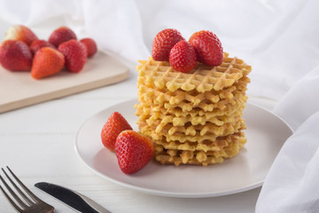 Delicious waffles with fresh fruit and berries on a white wooden table. Waffles with strawberries and blueberries. Free space for text. Traditional belgian waffles with fresh fruit. Stack of waffles w