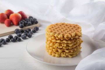 Delicious waffles with fresh fruit and berries on a white wooden table. Waffles with strawberries and blueberries. Free space for text. Traditional belgian waffles with fresh fruit. Stack of waffles w