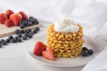 Delicious waffles with fresh fruit and berries on a white wooden table. Waffles with strawberries and blueberries. Free space for text. Traditional belgian waffles with fresh fruit. Stack of waffles w