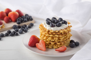 Delicious waffles with fresh fruit and berries on a white wooden table. Waffles with strawberries and blueberries. Free space for text. Traditional belgian waffles with fresh fruit. Stack of waffles w