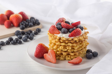 Delicious waffles with fresh fruit and berries on a white wooden table. Waffles with strawberries and blueberries. Free space for text. Traditional belgian waffles with fresh fruit. Stack of waffles w