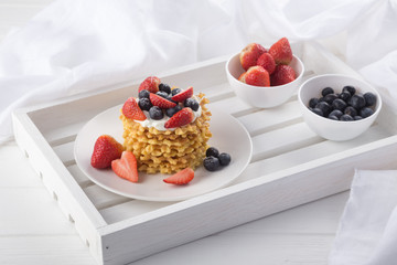 Delicious waffles with fresh fruit and berries on a white wooden table. Waffles with strawberries and blueberries. Free space for text. Traditional belgian waffles with fresh fruit. Stack of waffles w