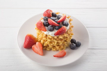 Delicious waffles with fresh fruit and berries on a white wooden table. Waffles with strawberries and blueberries. Free space for text. Traditional belgian waffles with fresh fruit. Stack of waffles w