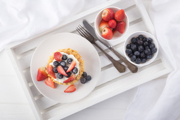 Delicious waffles with fresh fruit and berries on a white wooden table. Waffles with strawberries and blueberries. Free space for text. Traditional belgian waffles with fresh fruit. Stack of waffles w