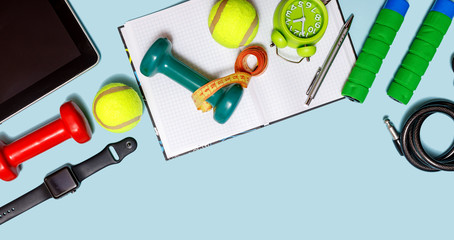 Healthy lifestyle concept with empty blank for text, fitness and sport. Tennis ball with dumbbells, alar clock and bottle of water isolated on pastel blue background.