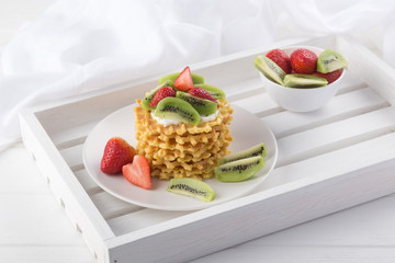 Delicious waffles with fresh fruit and berries on a white wooden table. Waffles with strawberries, kiwi, banana, cream. Free space for text. Traditional belgian waffles with fresh fruit. Stack of waff