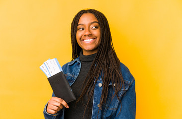Young african american woman holding a passport isolated looks aside smiling, cheerful and pleasant.