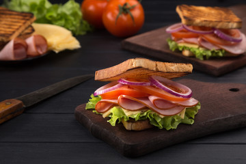Delicious sandwich with ham, cheese, lettuce, tomatoes, onion, sauce. High club sandwich with toast. close up of fresh sandwich with ham, bacon,tomatoes, cheese and lettuce On a wooden board. 