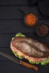 Delicious sandwich on a black wooden table. Sandwich with meat, ham, cheese, lettuce, tomatoes, onion, sauce. Close-up shot. Sandwich bread tomato, lettuce and yellow cheese. Free space for text.