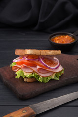 Delicious sandwich with ham, cheese, lettuce, tomatoes, onion, sauce. High club sandwich with toast. close up of fresh sandwich with ham, bacon,tomatoes, cheese and lettuce On a wooden board. 