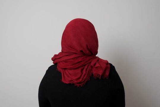 The Back View Of A Muslim Woman Wearing Hijab And Shiny Hair Standing Against Gray Wall. Studio Shoot.