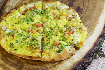 Sliced vegetarian pizza with tomatoes, broccoli and cheese on a wooden stand. Selective focus