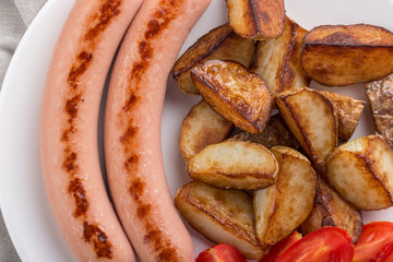 Close-up shot of fried potatoes with sausages and egg. Breakfast. Potatoes with sausages fried in oil, in rustic style. Frying pan with tasty cooked egg and sausages on table