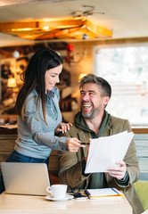 Portrait of young business man and woman at cafe discussing contract.