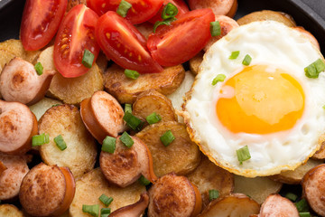 Close-up shot of fried potatoes with sausages and egg. Breakfast. Potatoes with sausages, cut into slices and fried in oil, in rustic style. Frying pan with tasty cooked egg and sausages on table