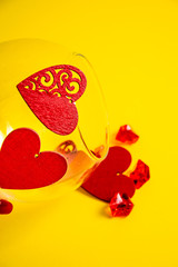 red crystals and hearts from a vase on a yellow background. composition of figures. valentine's day. vertical picture