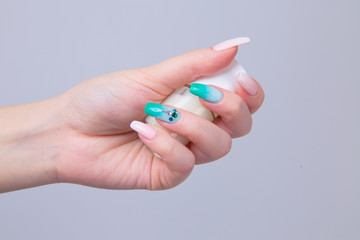 Art Manicure. Modern style pastel pink green Nail Polish with crystals. Beauty hands holding pastel white color bottle. Stylish Nails isolated purple background. Classic wedding bride nails design