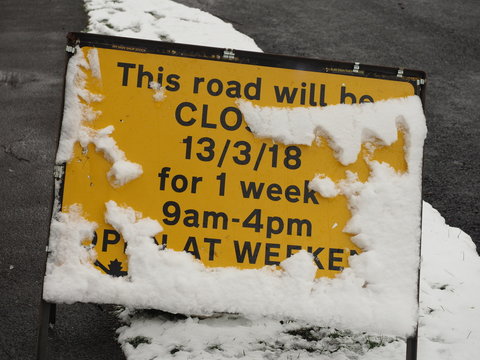 A Temporary Road Closure Sign Half Covered In Snow