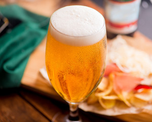 glass with chilled foamy beer on the background of snacks on the table