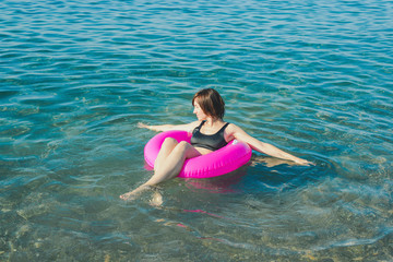 Young woman with pink swimming ring at the sea in sunny day. Summer vacation concept.