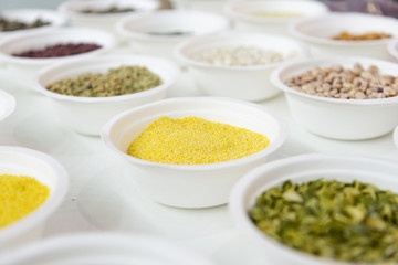 Millet in a white plastic plate. Around in the same plates are various seeds, nuts and beans.