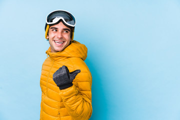 Young skier man wearing snowboard goggles isolated points with thumb finger away, laughing and carefree.