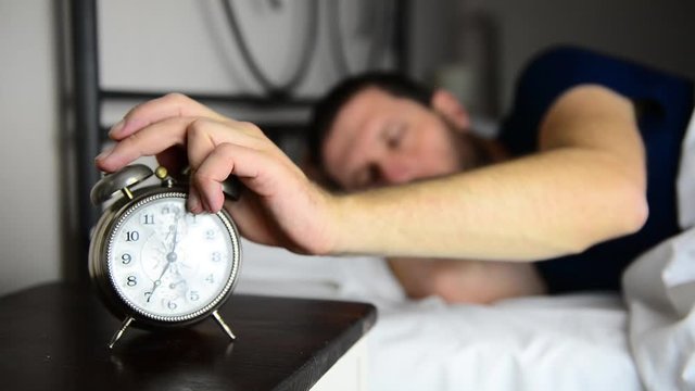 Closeup of caucasian man awaking at 7am, he stops the clock alarm with one hand