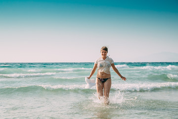 Fototapeta premium Young Caucasian Lady Woman In Swimsuit And Summer Hat Walking In Sea Water. Vacation On Sea Ocean Beach
