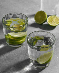 Water fitness detox with lime on a light grey background. Hard sun light and shadow. Soda coctail