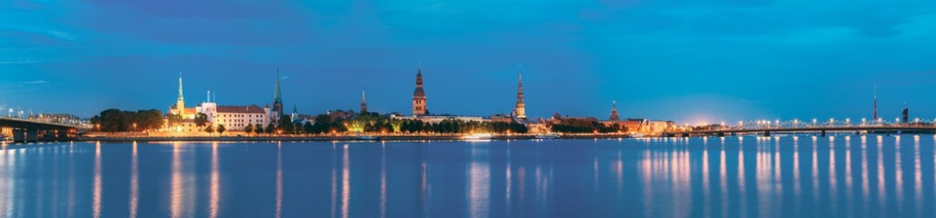 Fototapeta na wymiar Riga, Latvia. Panoramic Picturesque Urban View Of Daugava Or Western Dvina River In Central Part Of City With Famous Landmarks In Bright Illumination Under Blue Sky In Summer Night