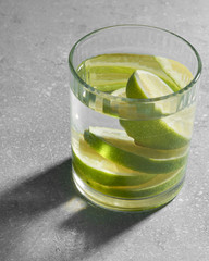 Water fitness detox with lime on a light grey background. Hard sun light and shadow. Soda coctail