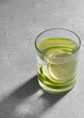 Water fitness detox with lime on a light grey background. Hard sun light and shadow. Soda coctail