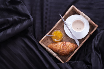 Cozy breakfast in bed, cup of coffee and croissants and jam