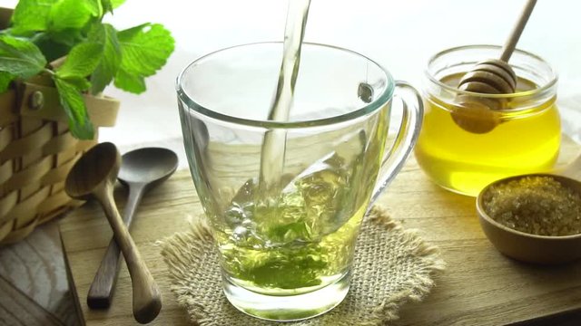 Mint tea being poured into cup. Slow motion shot. Honey in the background. Mint tea is a healthy source of vitamins such as manganese and a natural medicine.
