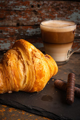Crisp chocolate croissant based on the dark plate with cappuccino