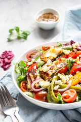 Vegetable salad cherry tomatoes, baked pepper, salad mix and onion with grilled haloumi (halloumi) cheese. Keto diet, healthy food. Light grey stone background.