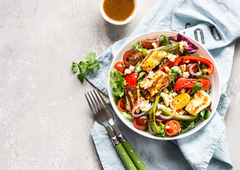Vegetable salad cherry tomatoes, baked pepper, salad mix and onion with grilled haloumi (halloumi) cheese. Keto diet, healthy food. Light grey stone background. Top view.